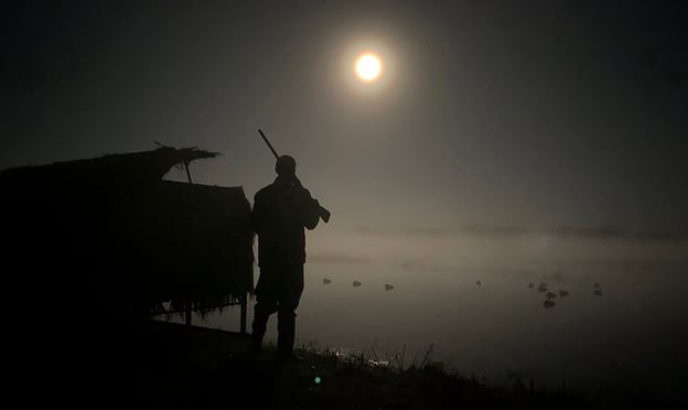 hunter standing by blind in moonlight